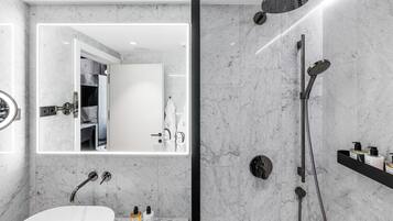 Une salle de bain moderne dotée d’un grand miroir, d’une baignoire sur pieds, d’une douche avec un pommeau de douche amovible et d’un meuble-lavabo avec des articles de toilette.