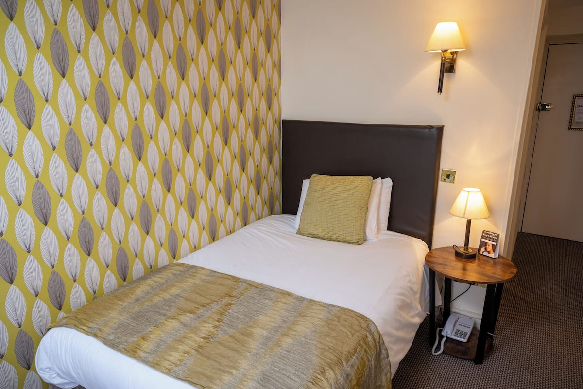 Une chambre d’hôtel avec un lit bien fait, une lampe de chevet et un téléphone sur une petite table placée à côté du lit.