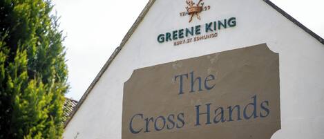 Un edificio con un letrero que dice "The Cross Hands" y "Greene King", con un emblema de corona.