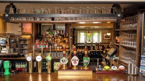 Een bar met verschillende biertaps, flessenrekken en glazen.