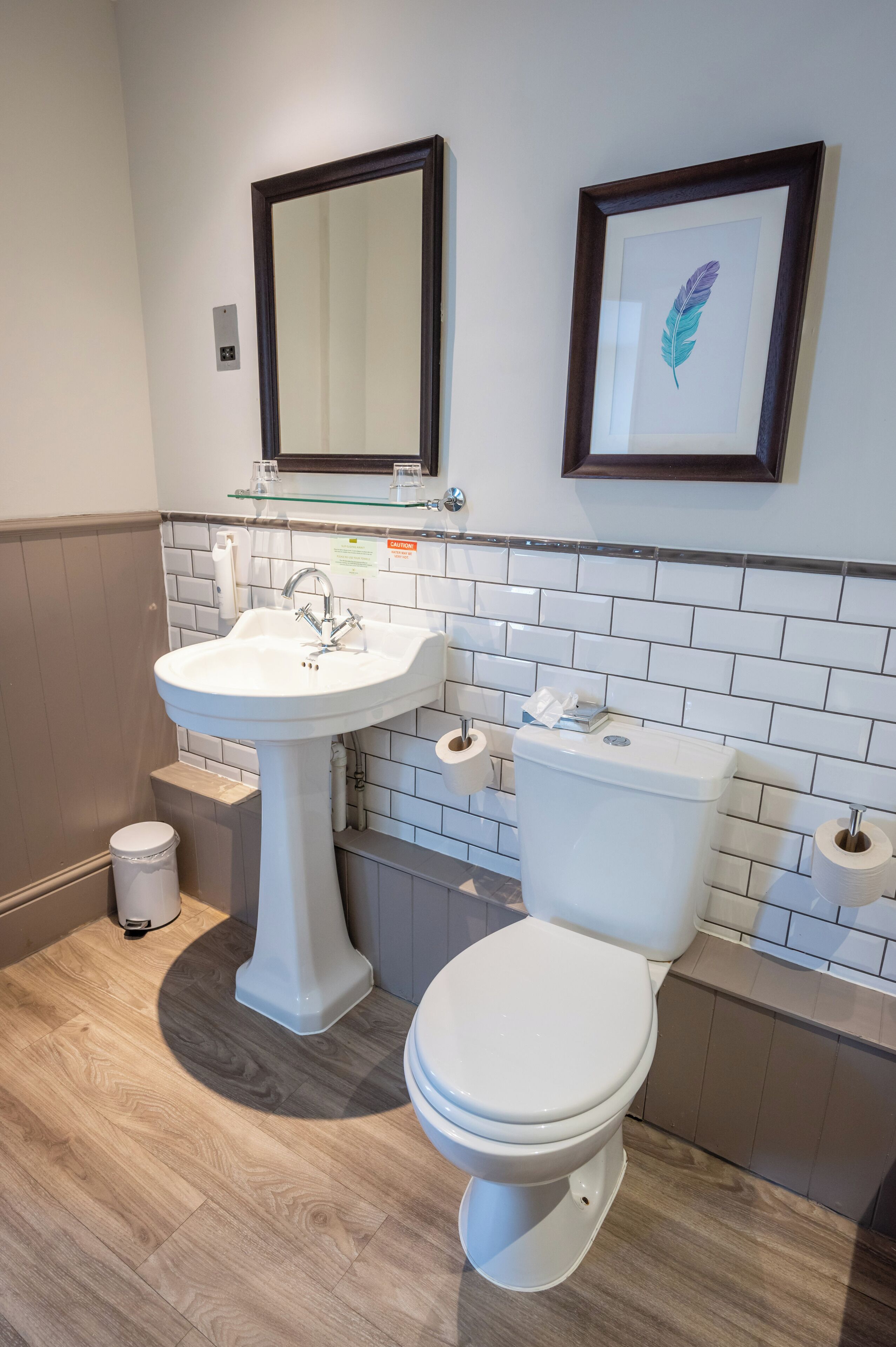 A bathroom with a pedestal sink, a toilet, and a framed feather artwork on the wall.