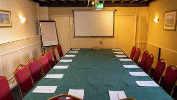 A conference room with a long table, red chairs, a projector screen, and a whiteboard.