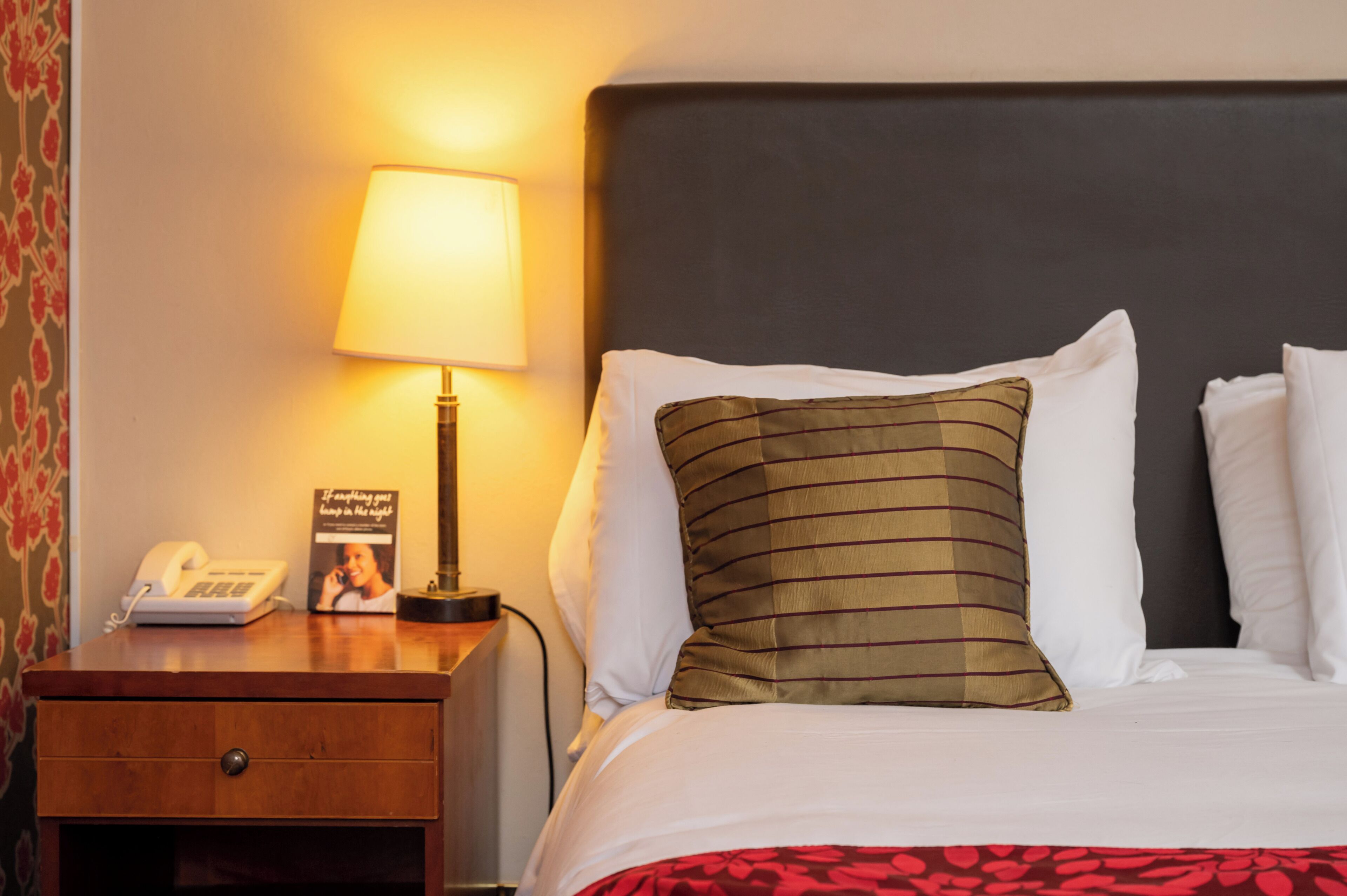 Een hotelkamer met een opgemaakt bed, een bedlampje, een telefoon en een ingelijste foto op het nachtkastje.