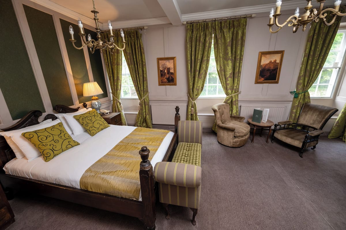 Une chambre d’hôtel avec un grand lit, un coin salon comprenant un fauteuil et une petite table, et deux tableaux accrochés au mur.