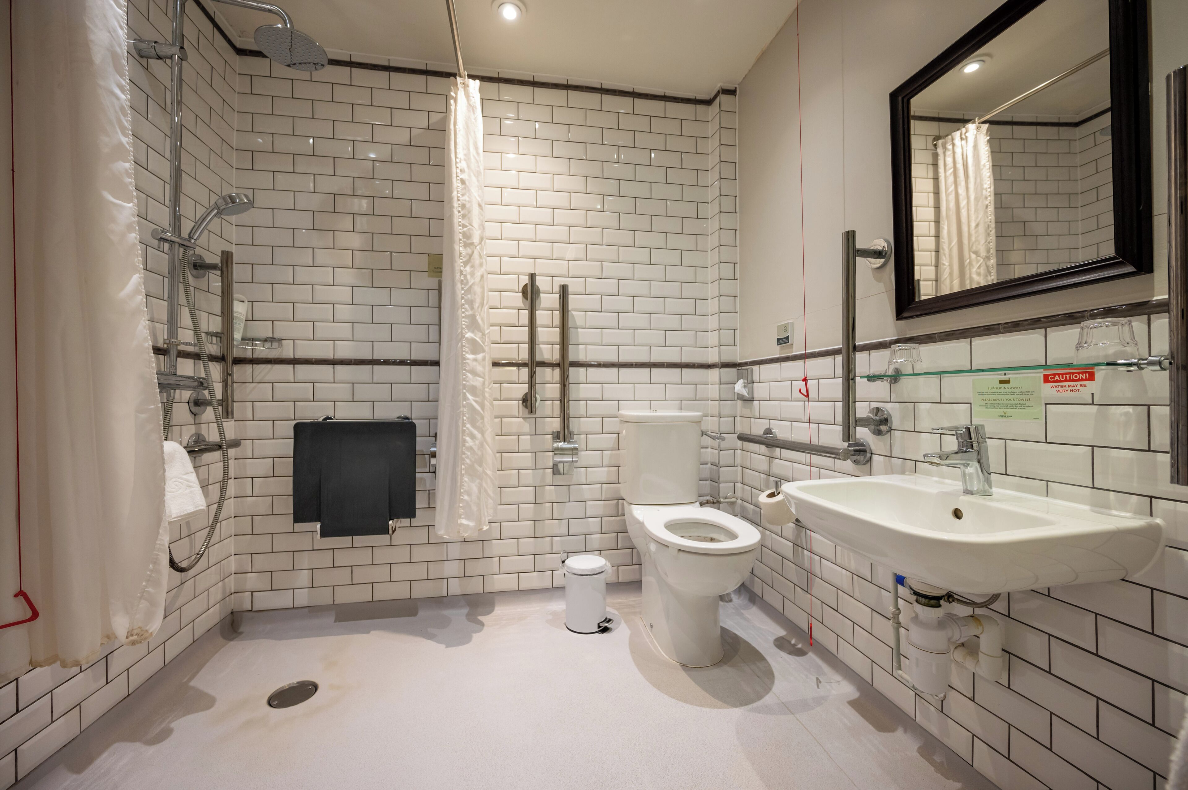 A modern bathroom with white subway tiles, a glass shower enclosure, a toilet, and a sink with a mirror above it.