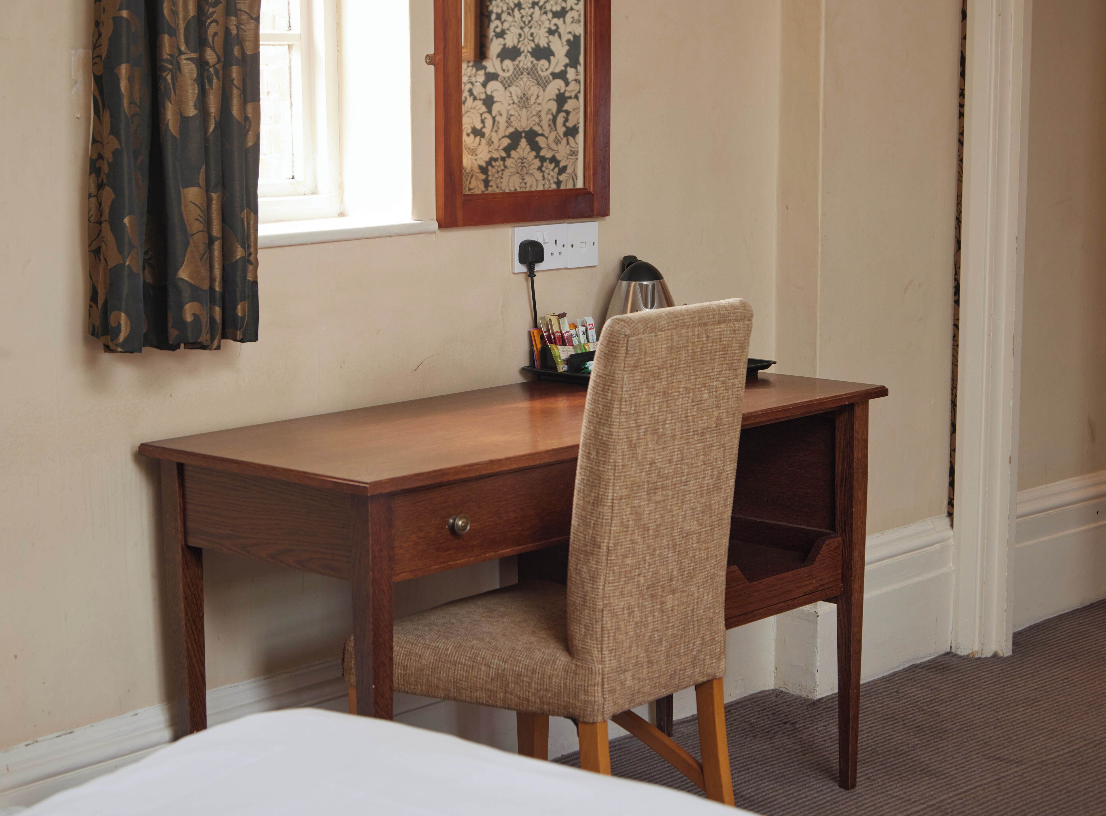 A wooden desk with a chair, a lamp, and a framed picture on the wall.