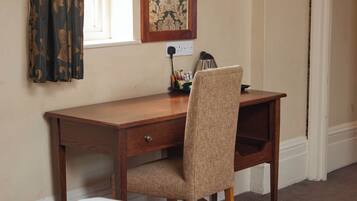A wooden desk with a chair, a lamp, and a framed picture on the wall.