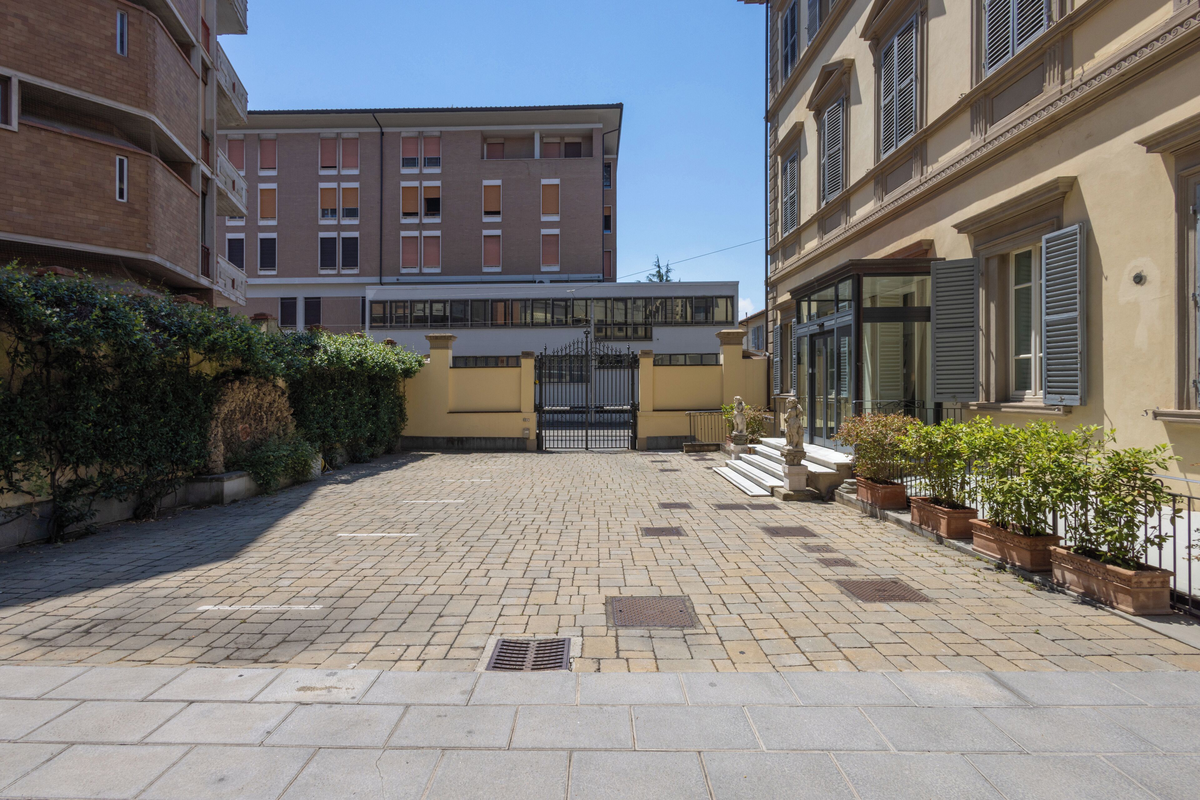 A courtyard with a paved walkway, a gated entrance, and buildings with balconies and windows.