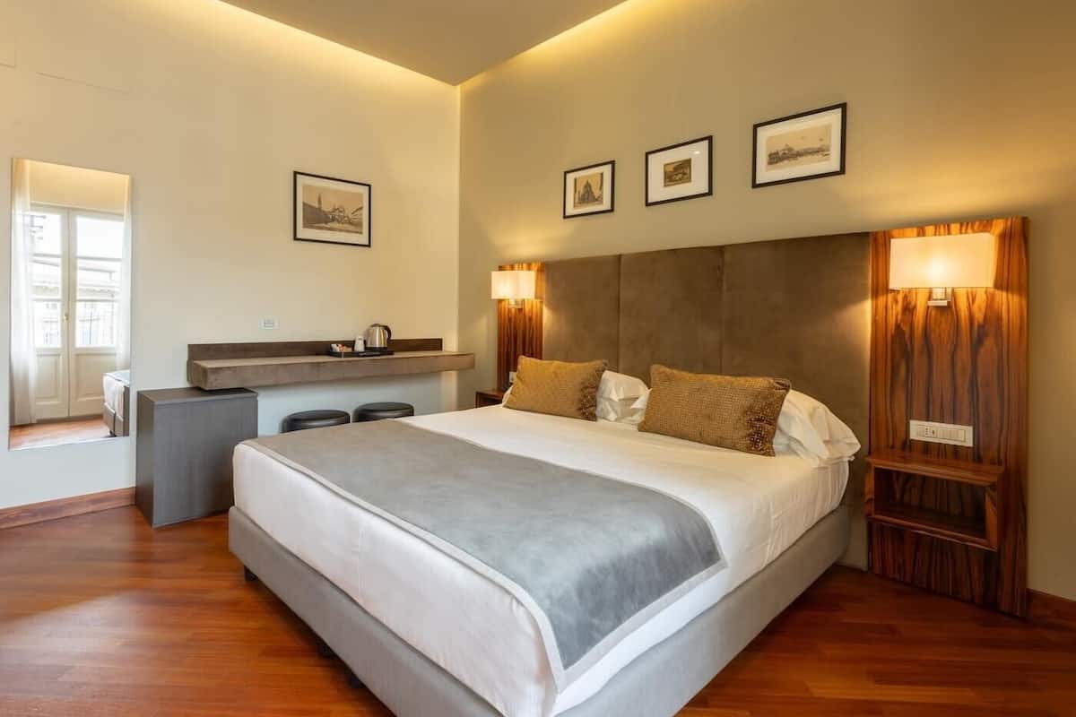 A modern hotel room with a large bed, bedside lamps, a desk, and a window with curtains.