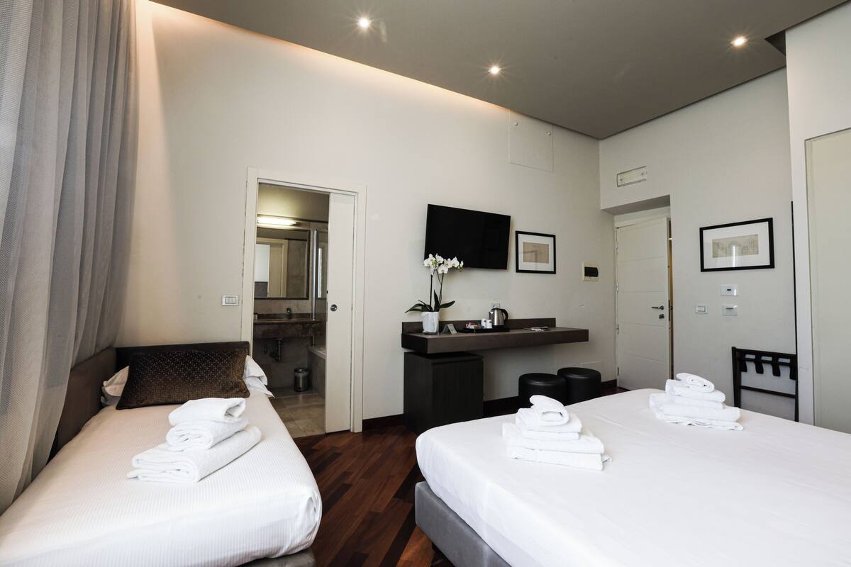 A hotel room with two beds, a bathroom, and a desk with a flat-screen TV.