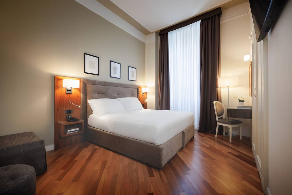 A hotel room with a large bed, wooden flooring, a desk with a chair, and a TV mounted on the wall.