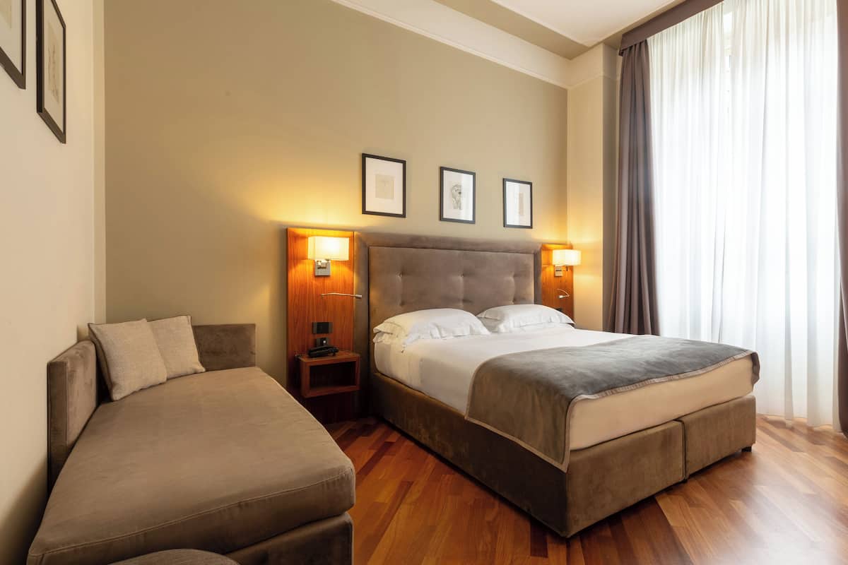 A hotel room with a large bed, a sofa, and two bedside lamps.