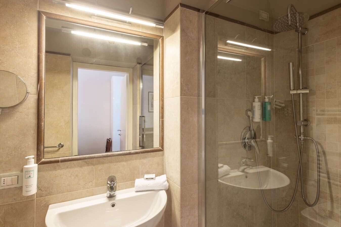 Een moderne badkamer met een douchecabine van glas, een wastafel met spiegel erboven en toiletartikelen aan de wand.