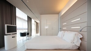 Una habitación de hotel moderna con una cama grande, un televisor sobre un mueble bajo, un escritorio y un armario.