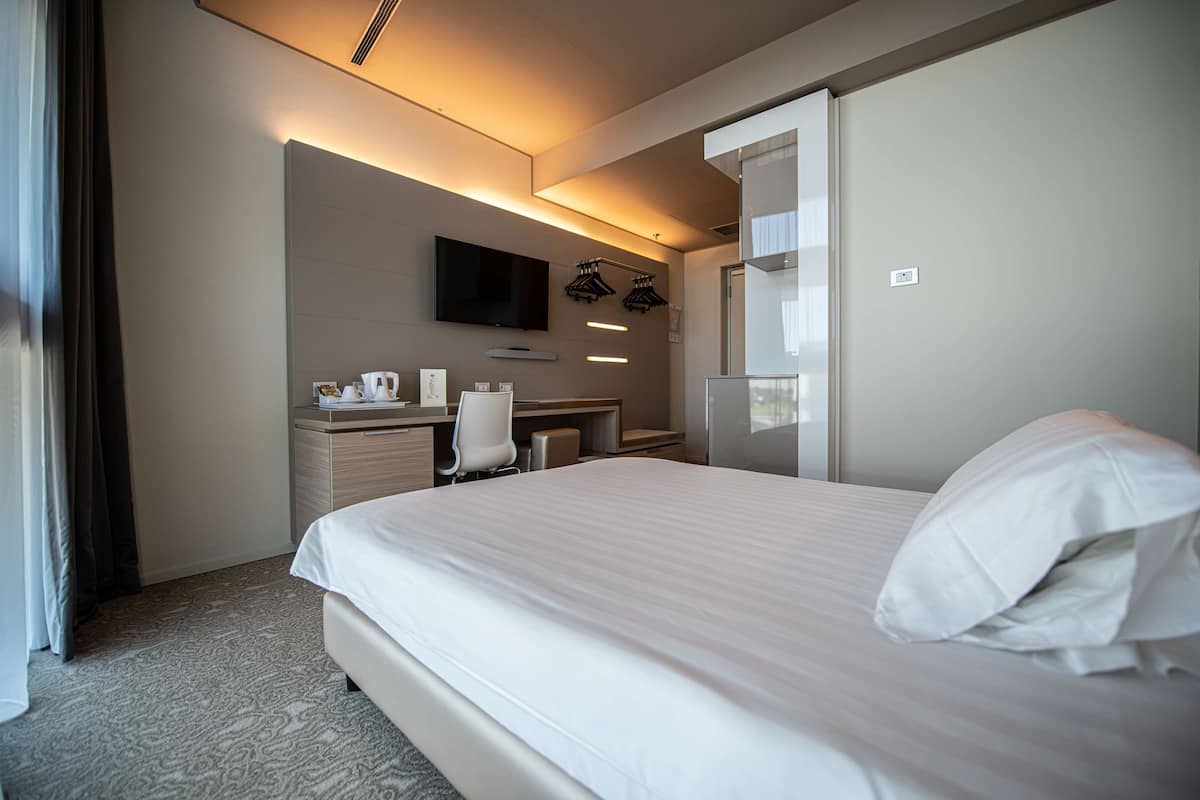 Hotellihuone, jossa on suuri sänky, työpöytä tuolilla, taulutelevisio ja peili.