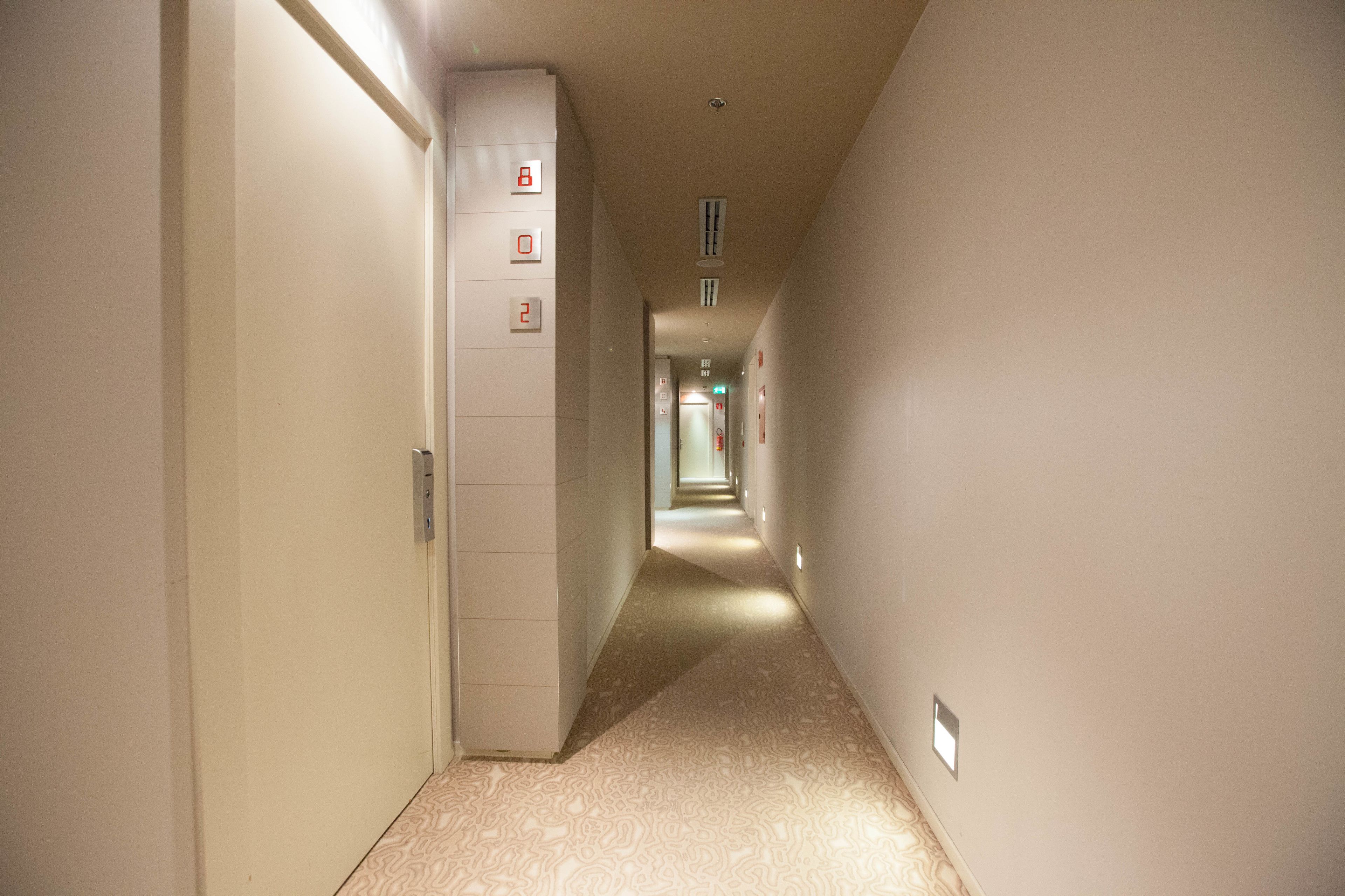 Un pasillo estrecho y bien iluminado con alfombra estampada y una puerta a la izquierda.