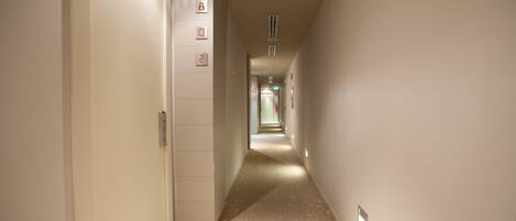 Un pasillo estrecho y bien iluminado con alfombra estampada y una puerta a la izquierda.