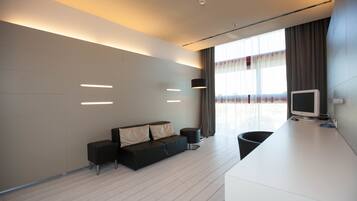 A modern hotel room with a sofa, a small table, a TV, and a large window with curtains.