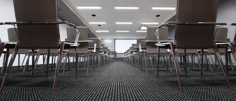 Un salón de conferencias con filas de sillas orientadas hacia una pantalla de proyección.