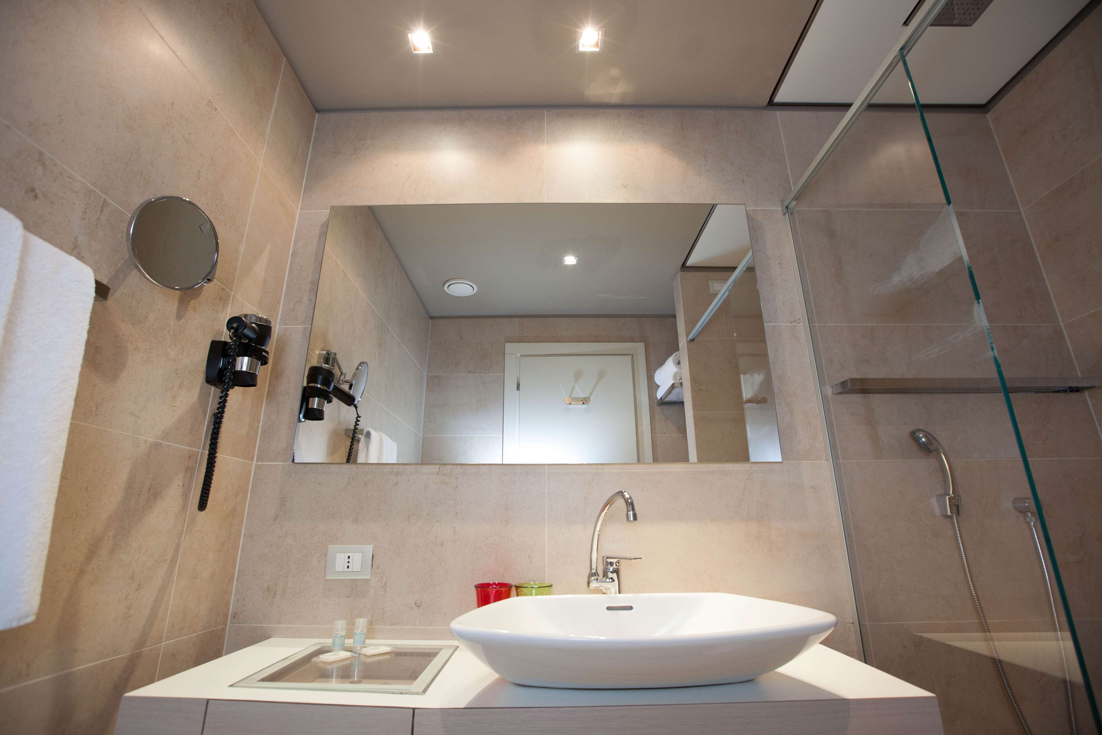 A modern bathroom with a large mirror, a white sink, and a glass-enclosed shower.