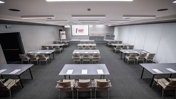 A conference room with multiple tables and chairs, a projector screen displaying 'NET TOWER', and a presentation podium.