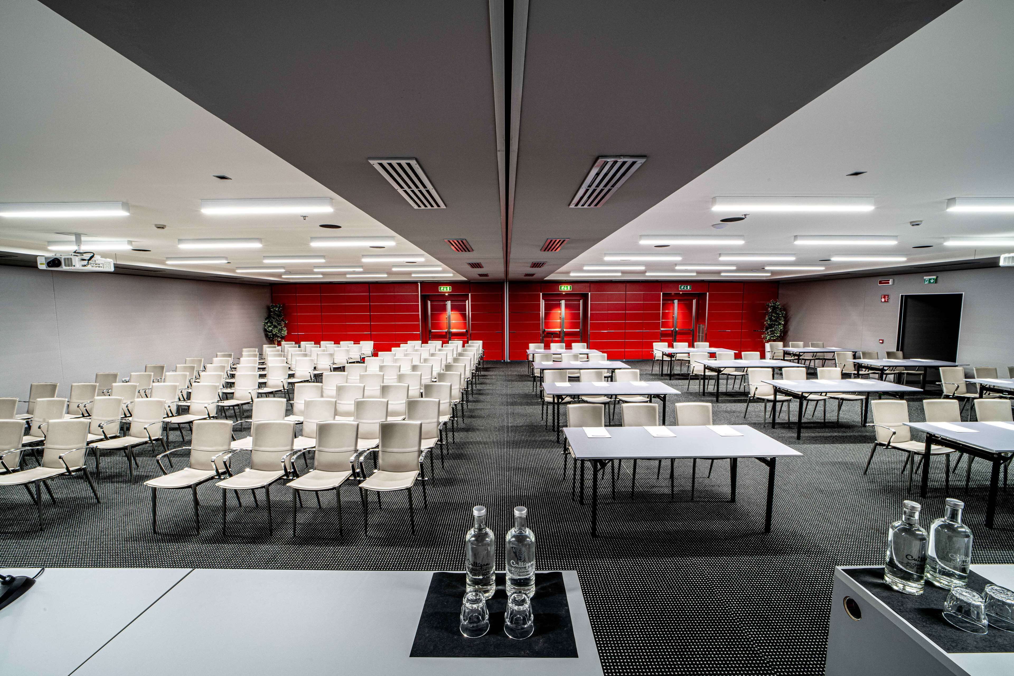 A conference room with rows of chairs and tables, equipped with projectors and a large screen.