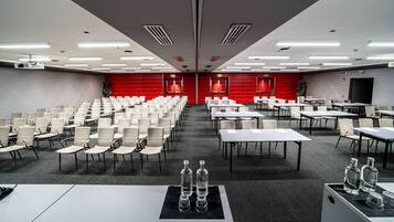Ein Konferenzraum mit Tischen und Stuhlreihen, ausgestattet mit Projektoren und einer großen Leinwand.