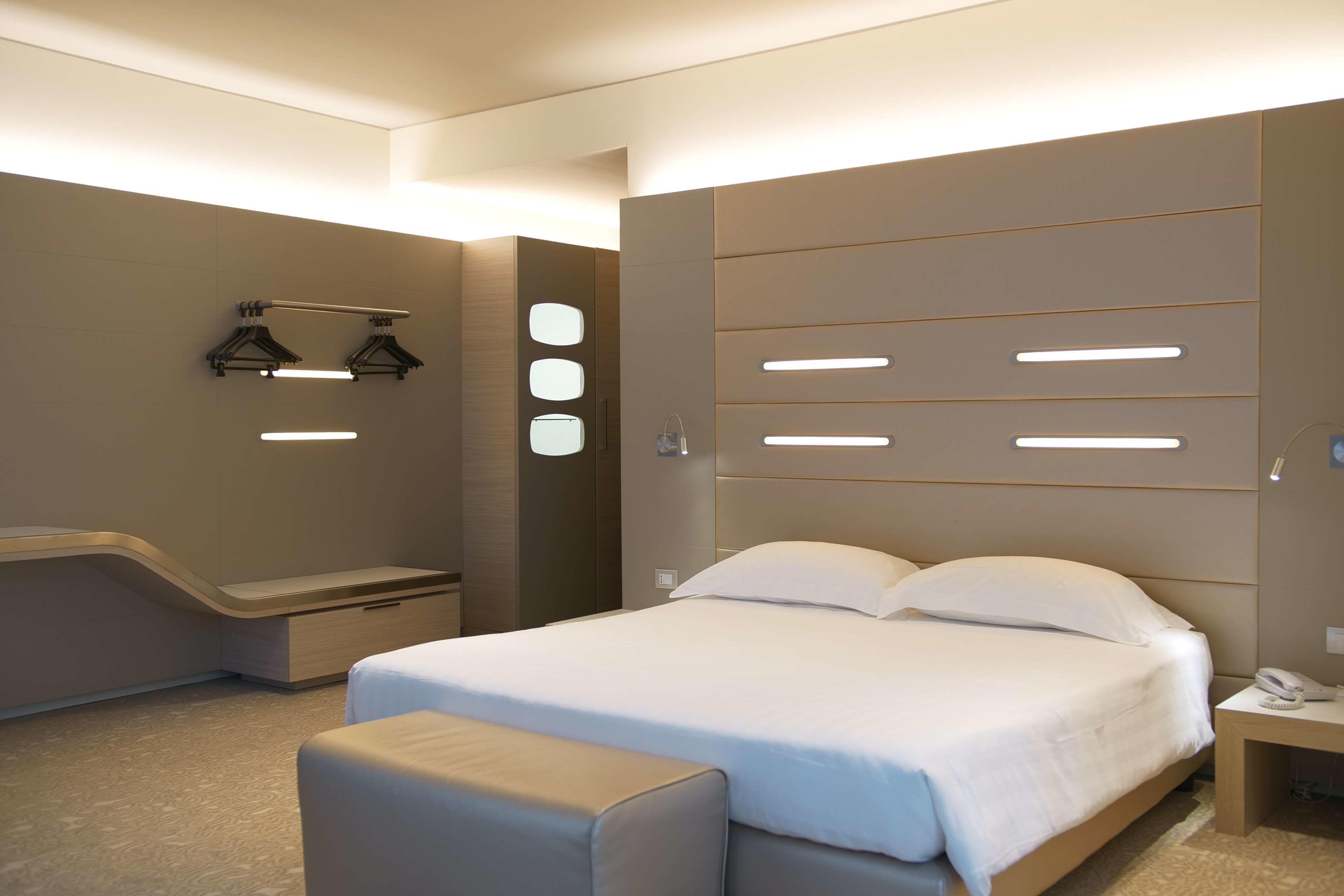 Une chambre d’hôtel moderne dotée d’un grand lit, de tables de chevet, d’un banc et d’un éclairage intégré.