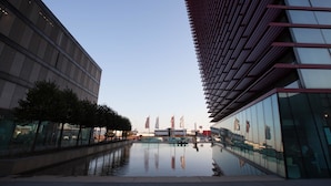 Un edificio moderno con una fuente reflectante frente a él, amplios ventanales y cielo despejado.