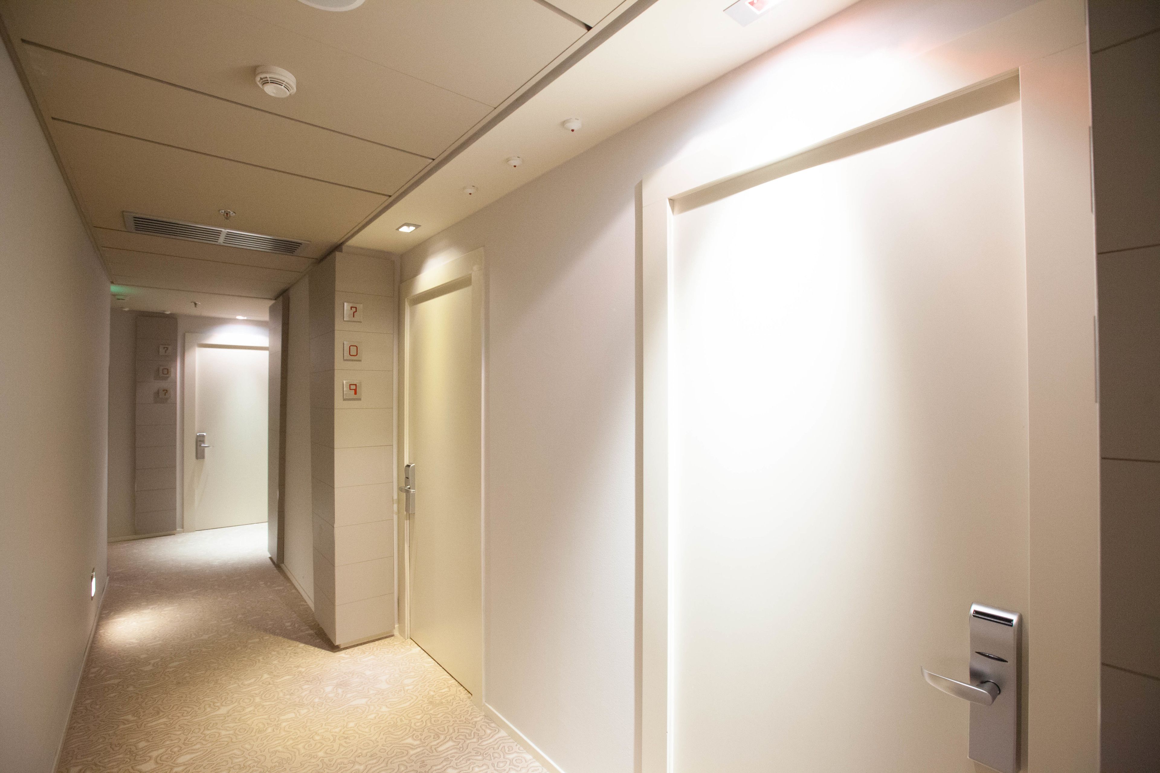 A hallway with a door on the right, a door with a number on the left, and a light fixture on the ceiling.