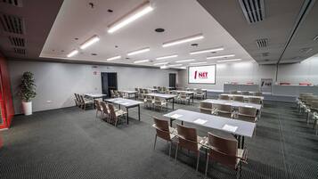 Une salle de conférence équipée de tables et de chaises, d’un écran de projection et d’une plante.