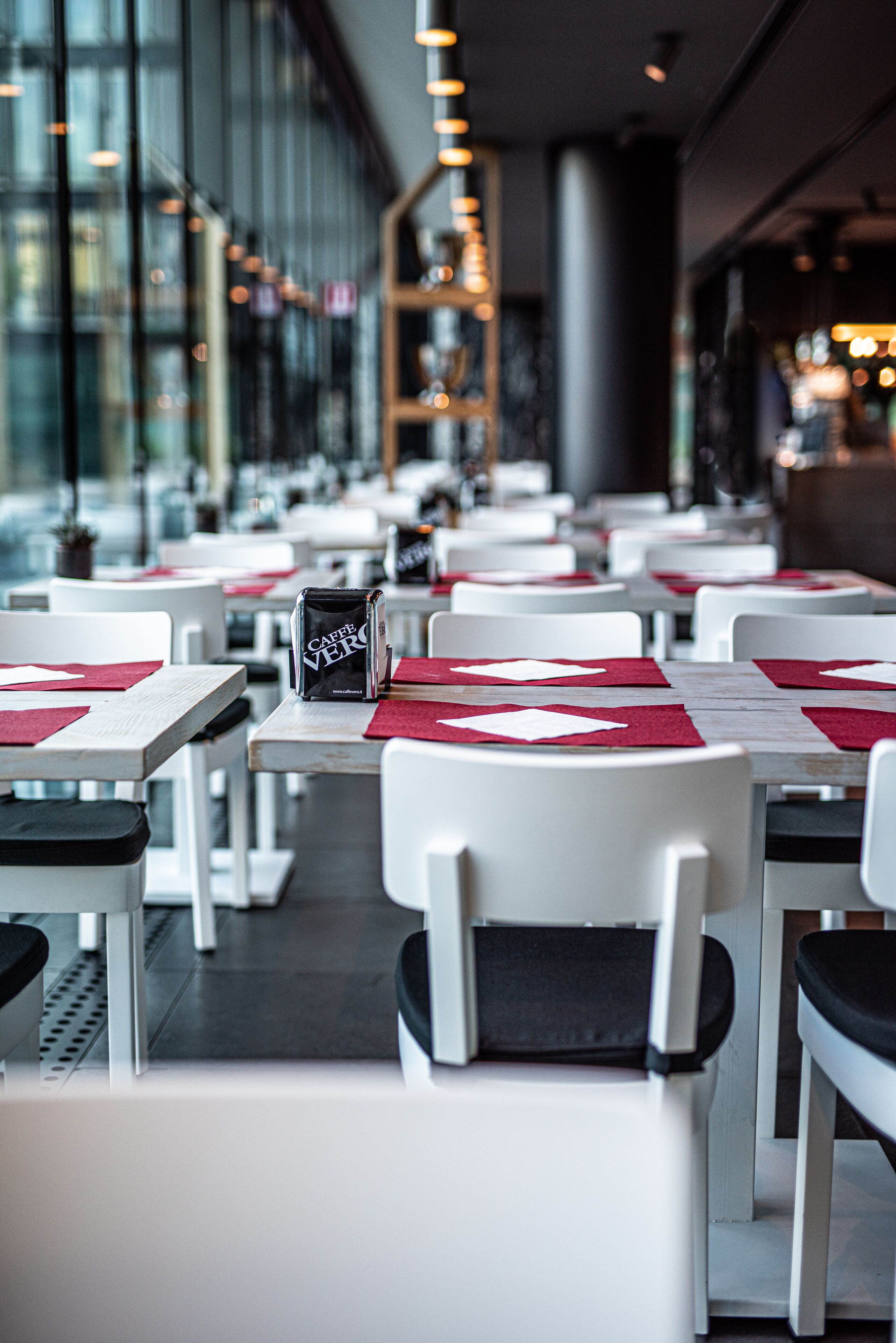 A restaurant with white tables and chairs, red placemats, and a menu stand.