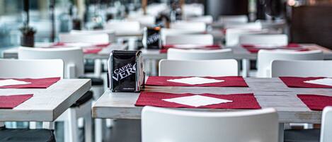 A restaurant with white tables and chairs, red placemats, and a menu stand.