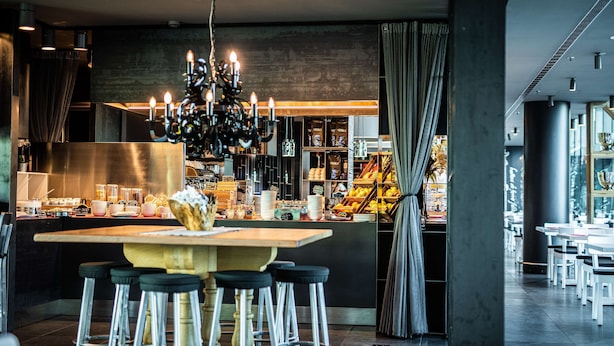 Un área de bar moderna con una isla central, taburetes de bar, una araña y vista de la cocina al fondo.