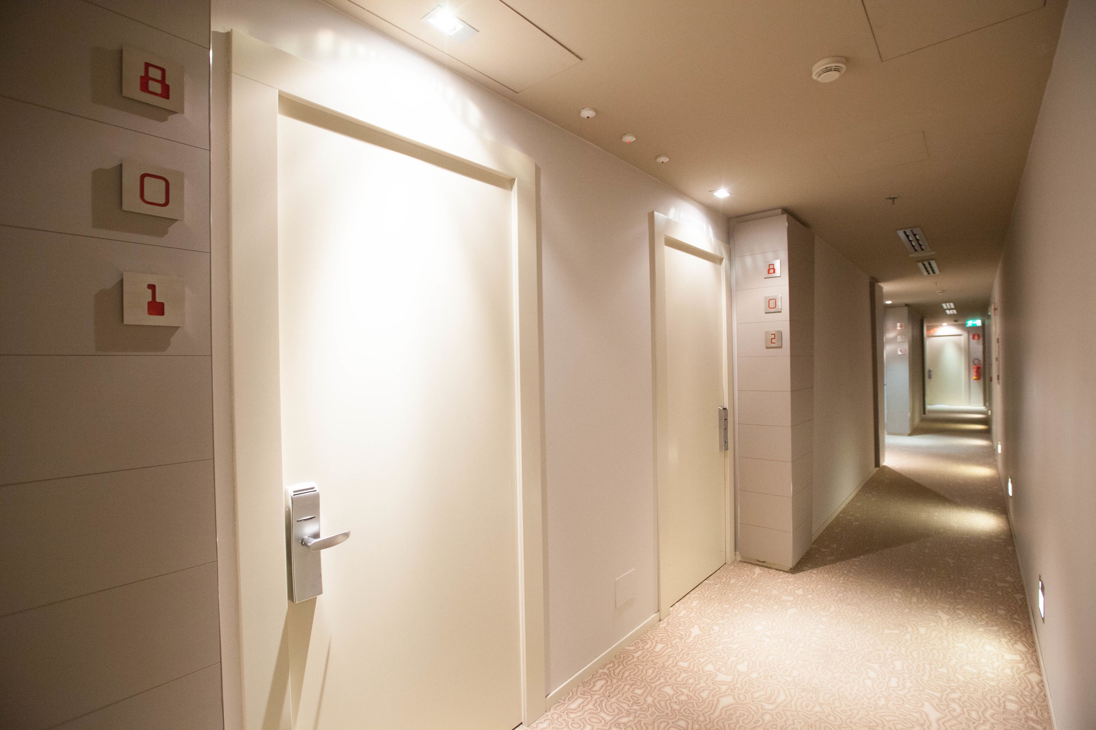 A hotel corridor with doors, emergency exit signs, and a patterned carpet.