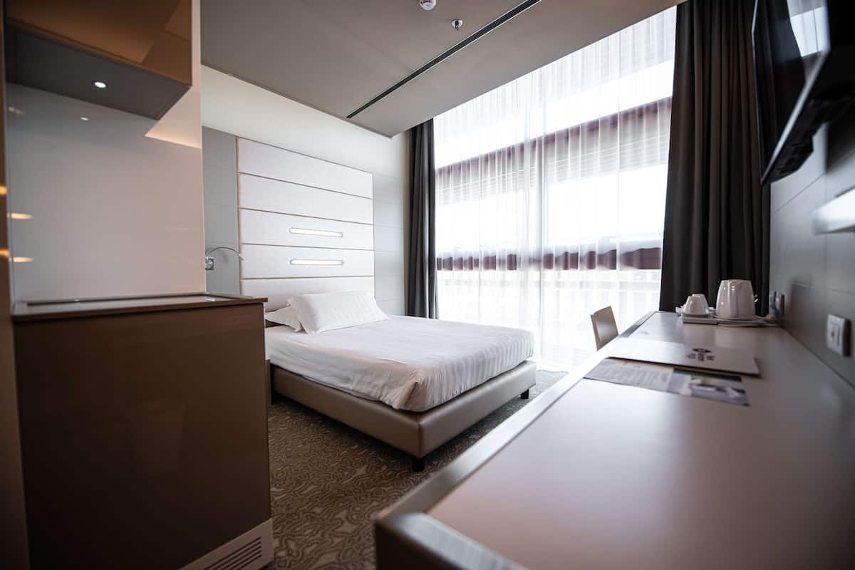 Moderni hotellihuone, jossa on siististi pedattu sänky, työpöytä tuolilla ja suuri ikkuna, jossa on verhot.
