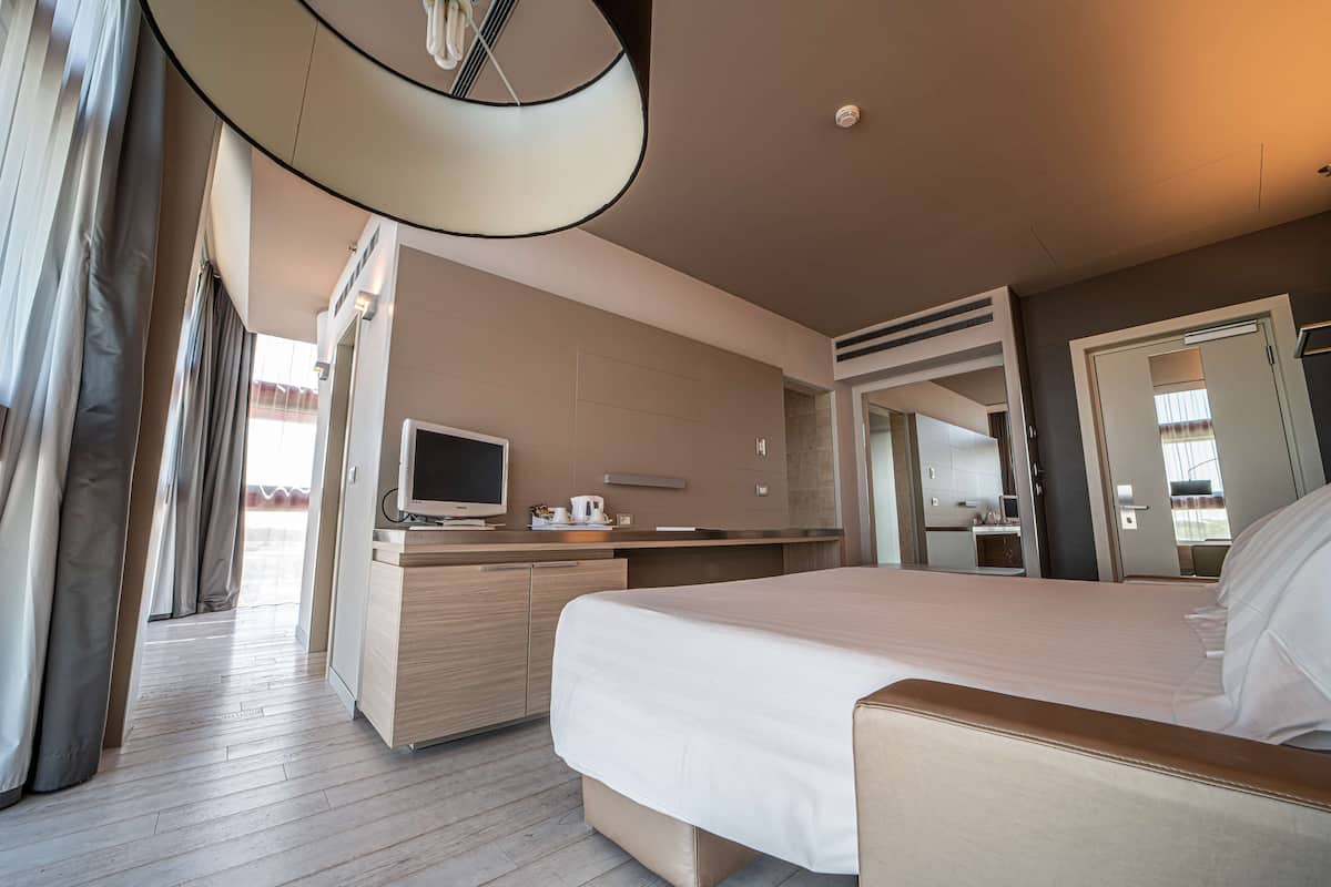 Moderni hotellihuone, jossa on suuri sänky, televisio, työpöytä ja kylpyhuone, joka näkyy avoimesta ovesta.