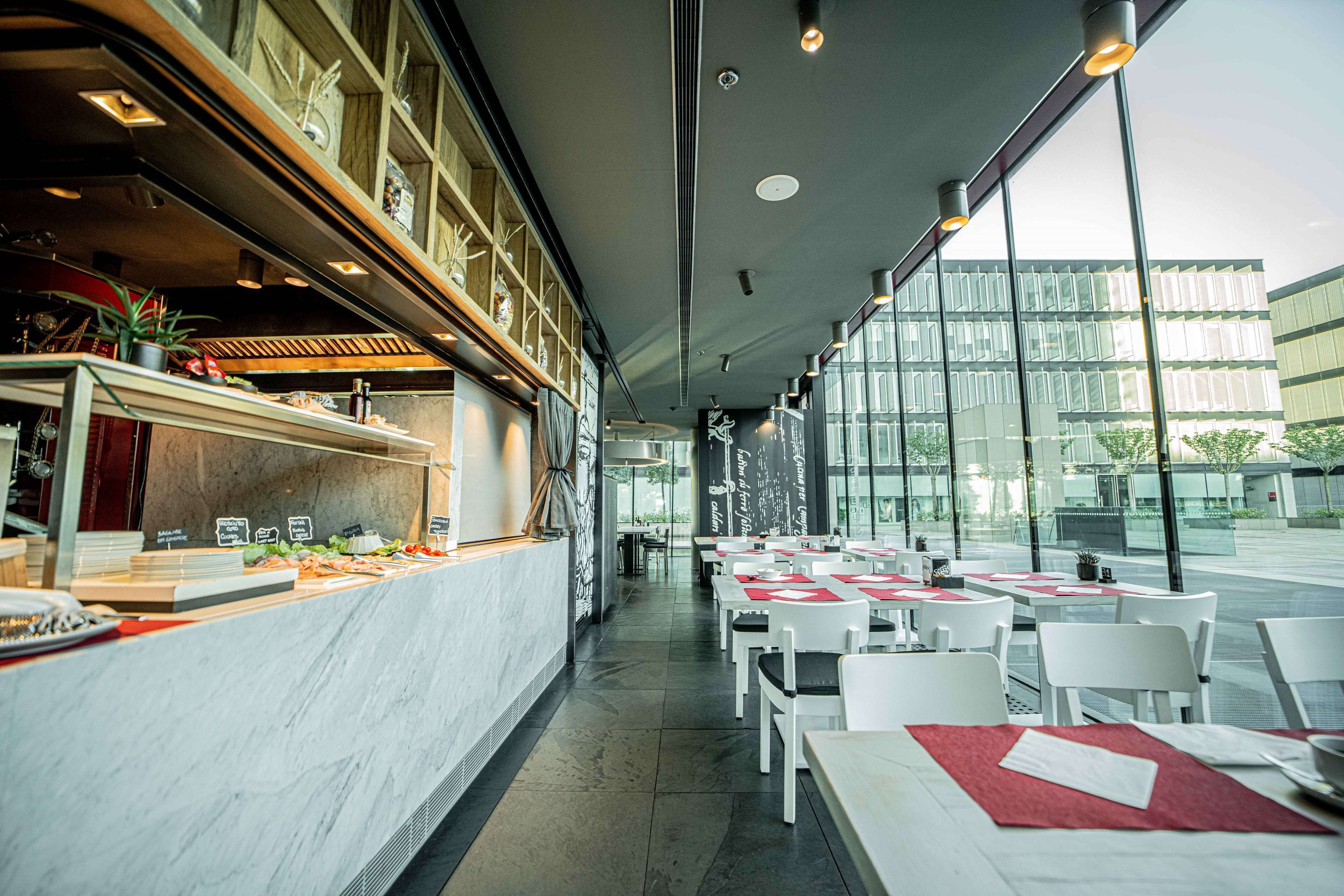 A modern restaurant with a marble counter, white tables, and a view of a glass building.