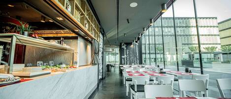 A modern restaurant with a marble counter, white tables, and a view of a glass building.