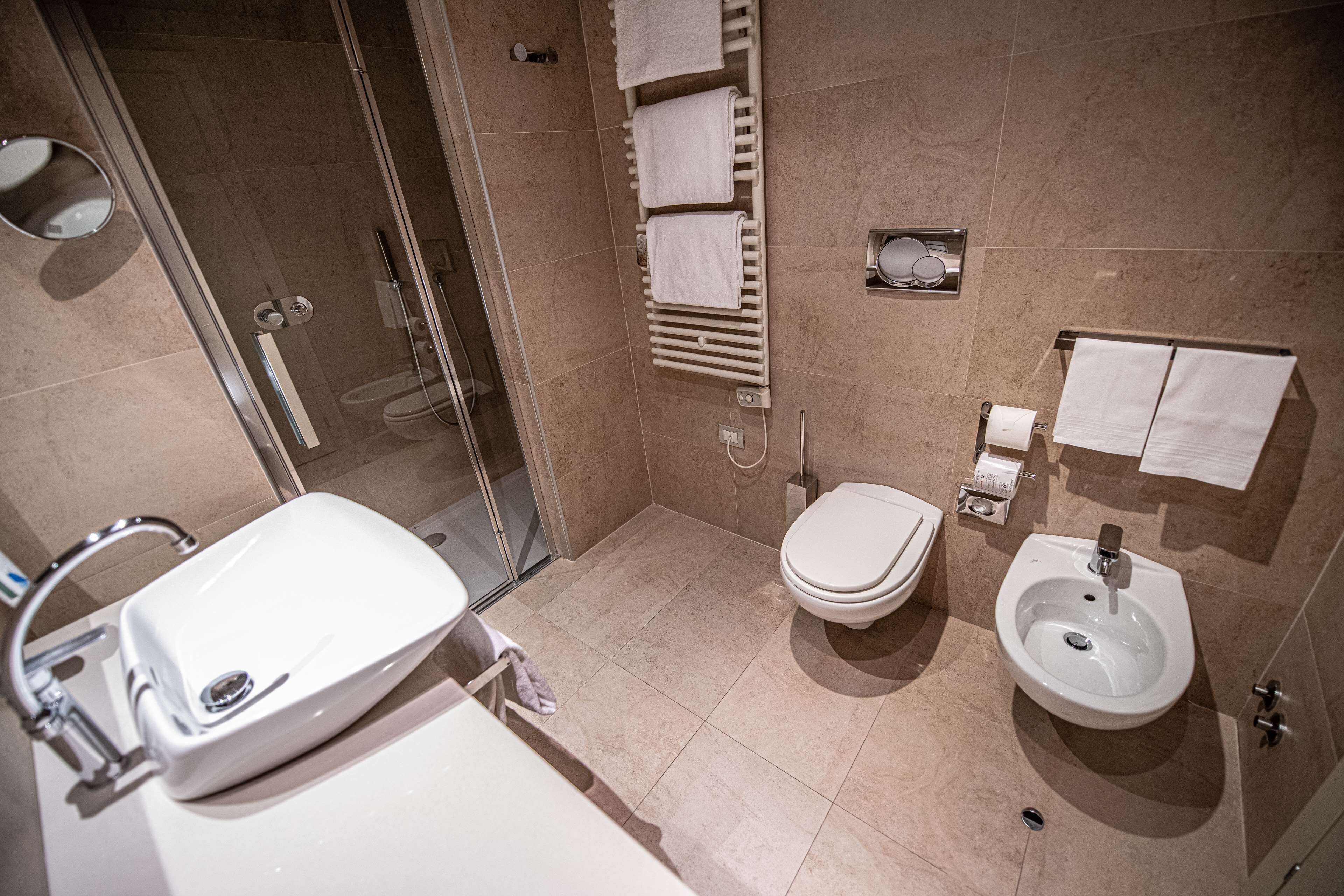 A modern bathroom with a glass-enclosed shower, a white sink, a toilet, and a bidet.
