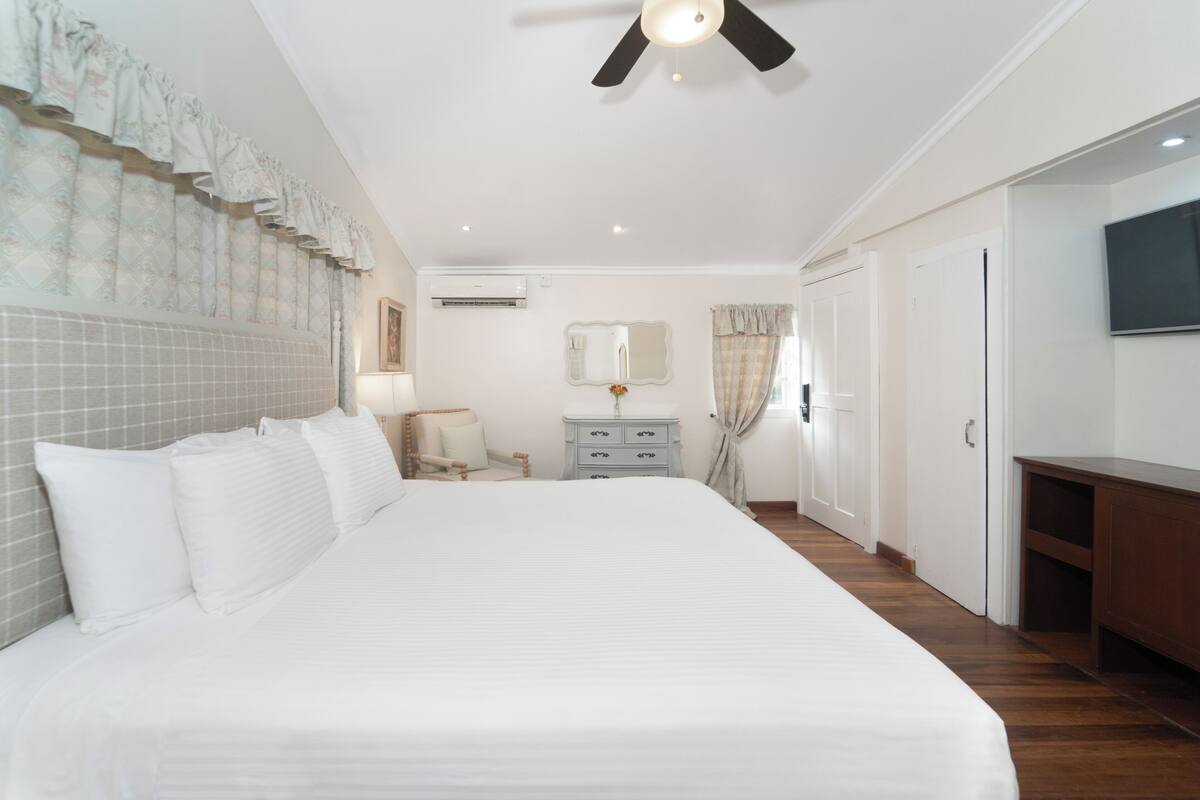 A bedroom with a large bed, a ceiling fan, a dresser, a mirror, and a TV on the wall.