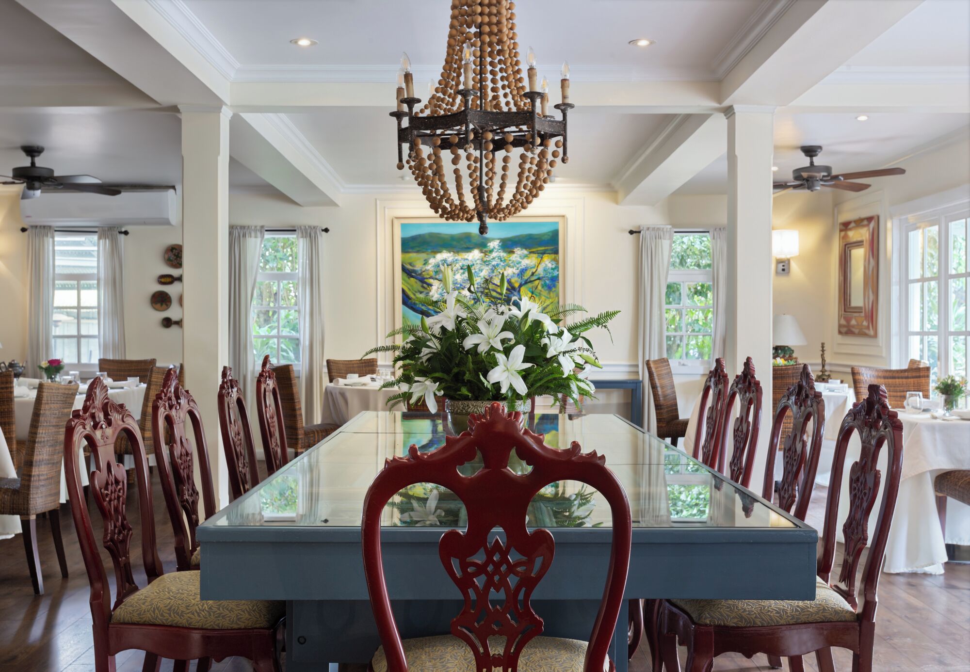 A dining room with a large glass table, wooden chairs, and a chandelier.
