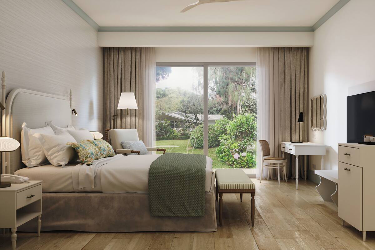 A hotel room with a bed, bedside table, lamp, chair, desk, TV, and a view of the garden.