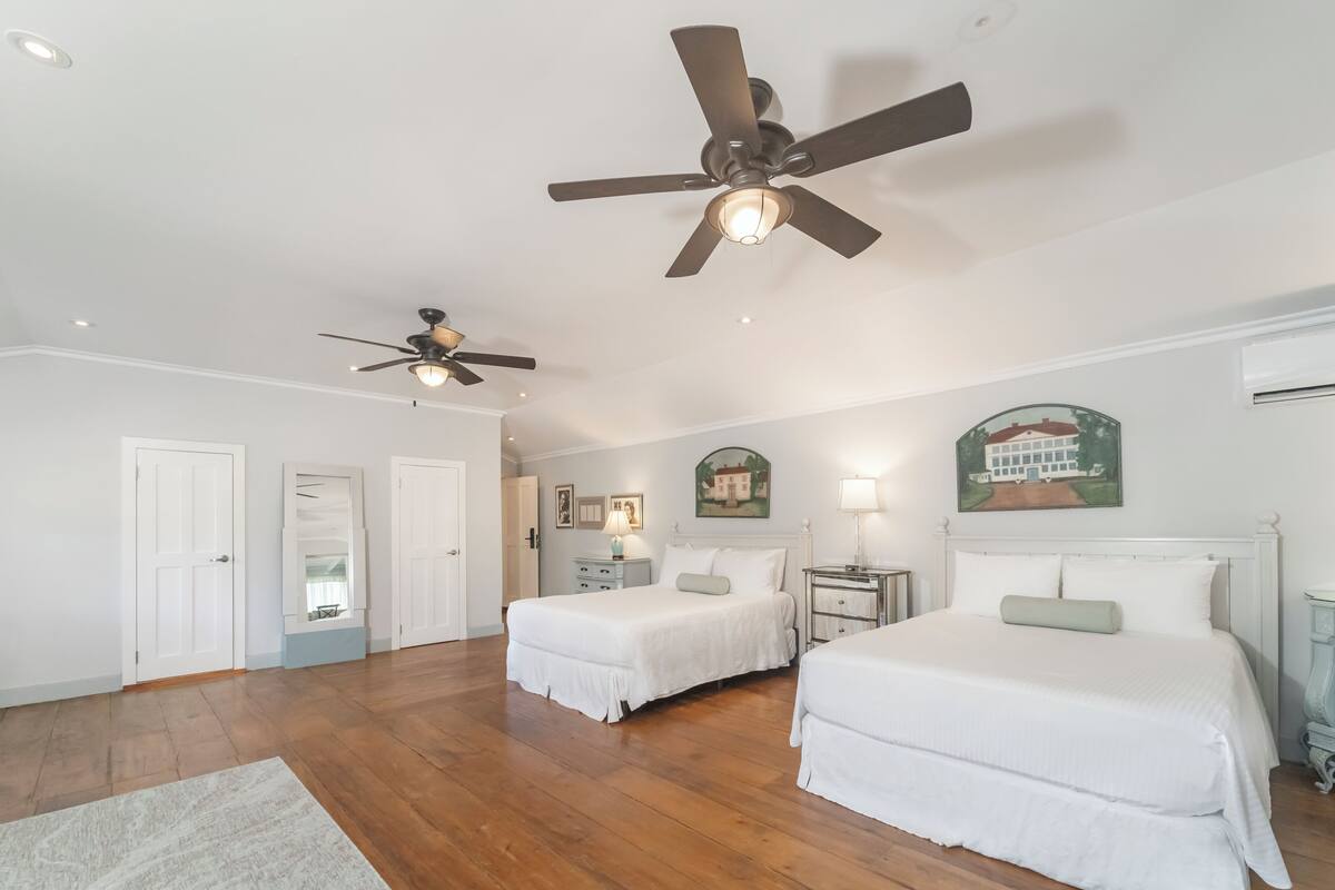A bedroom with two beds, ceiling fans, a nightstand, and a wall-mounted lamp.