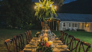 An outdoor dining area with a long table set for a meal, surrounded by chairs, under a tree with hanging lights. - Hotel Panamonte (Jaramillo)
