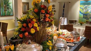 A buffet setup with various food stations, a large floral centerpiece, and a dining area with tables and chairs.