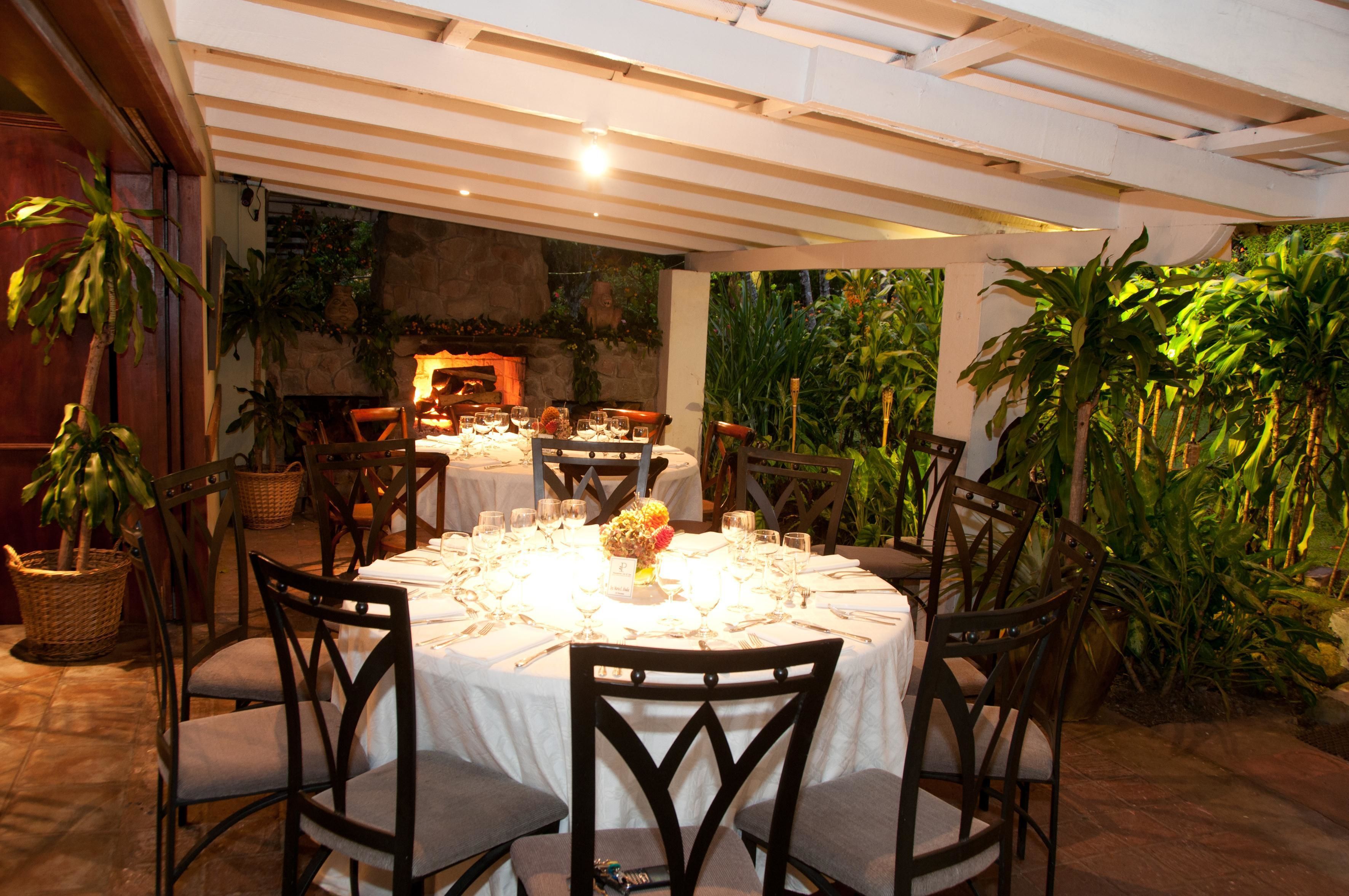 A dining area with round tables set for multiple guests, surrounded by chairs and potted plants.