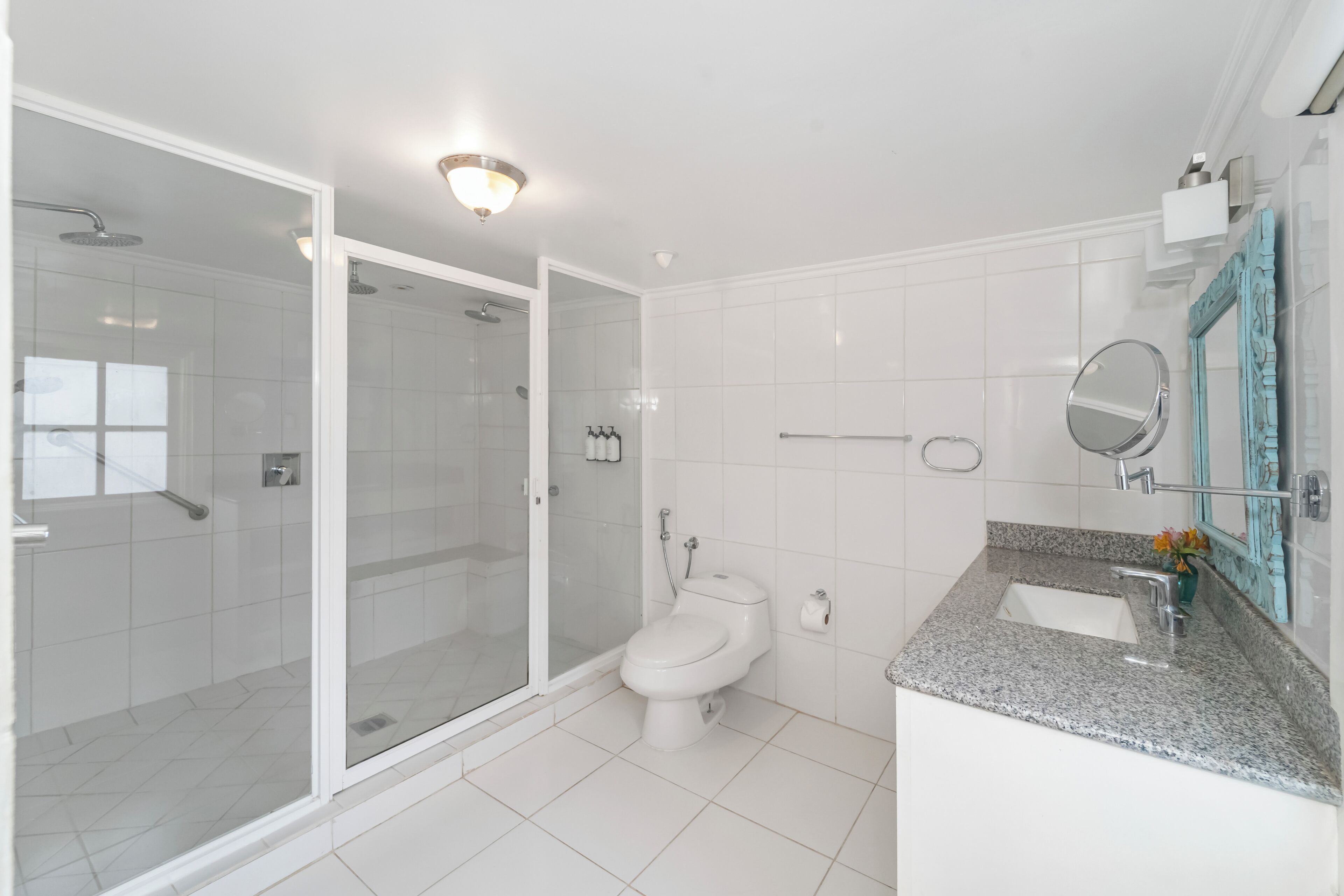 A modern bathroom with a glass-enclosed shower, a white toilet, a granite countertop sink, and a mirror with a decorative frame.