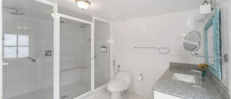 A modern bathroom with a glass-enclosed shower, a white toilet, a granite countertop sink, and a mirror with a decorative frame.