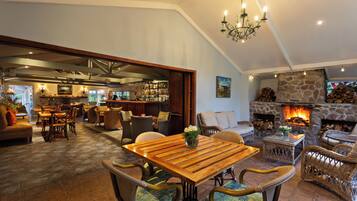 Amplia sala de estar con mesa de comedor de madera, mobiliario de mimbre, chimenea de piedra y zona de bar con vistas al exterior.